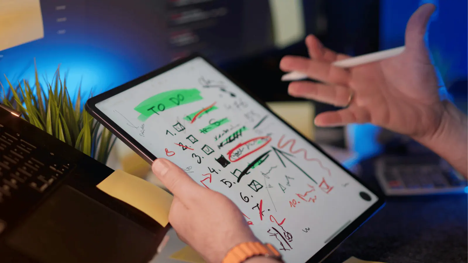 Hands holding tablet displaying handwritten to-do list with stylus and desk items