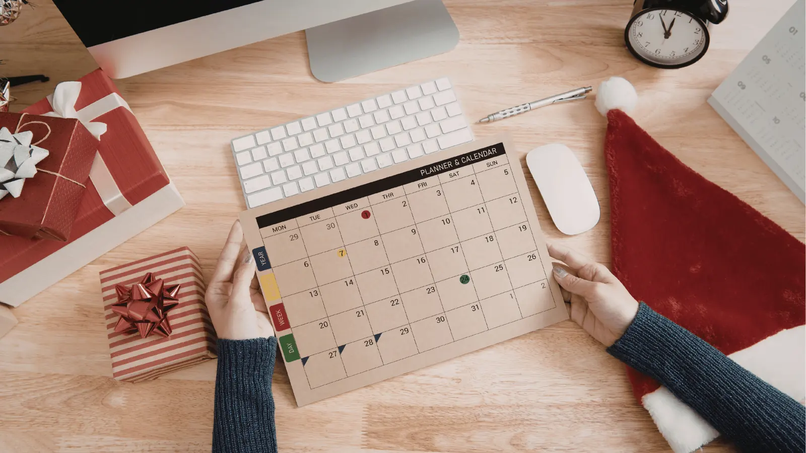 Hands holding a paper monthly planner on a wooden desk with gifts for content calendar