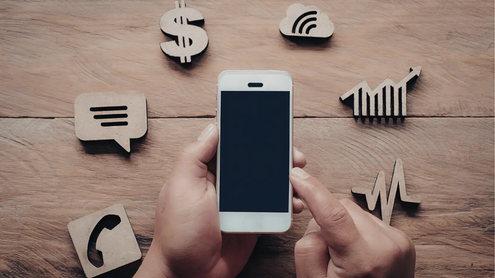 Hand holding smartphone over wooden table surrounded by wooden app icons