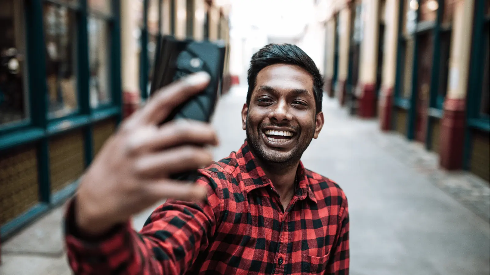 Smiling man in red plaid shirt taking a selfie with smartphone for AI-assisted workflow
