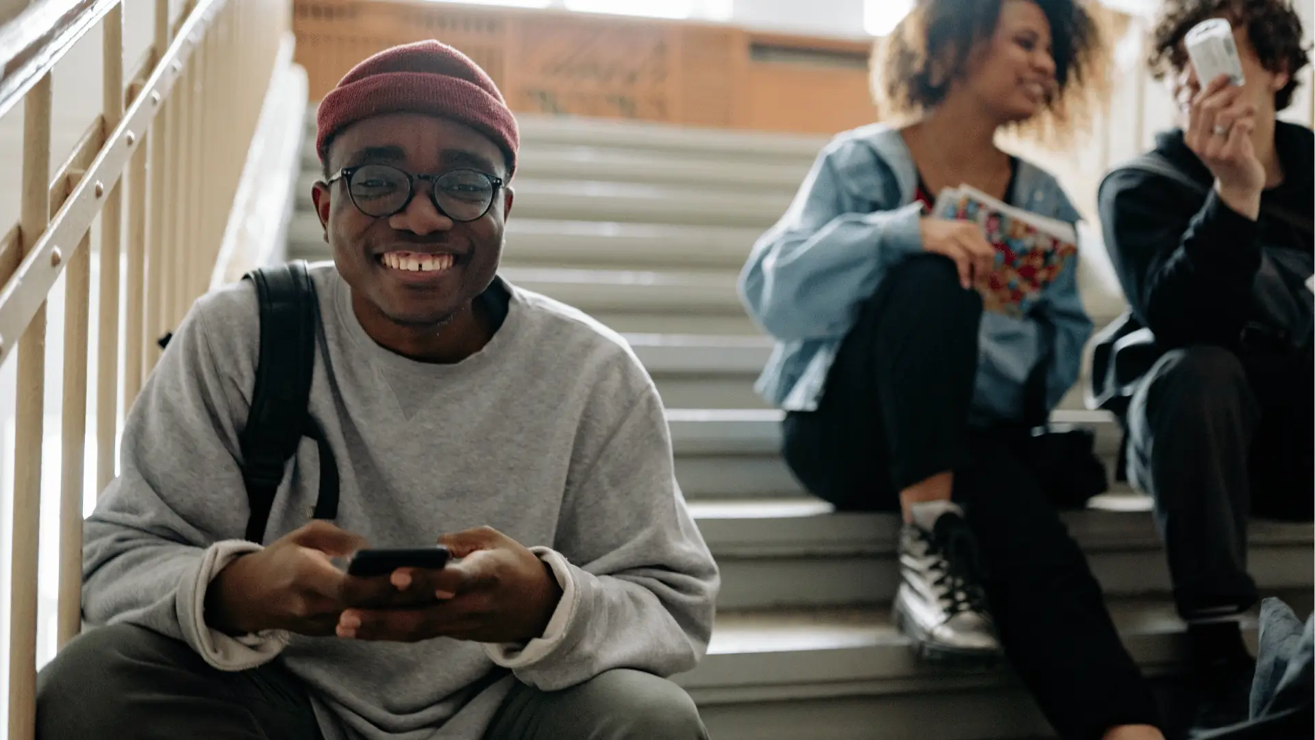 Smiling young man on stairs holding a phone with friends behind him