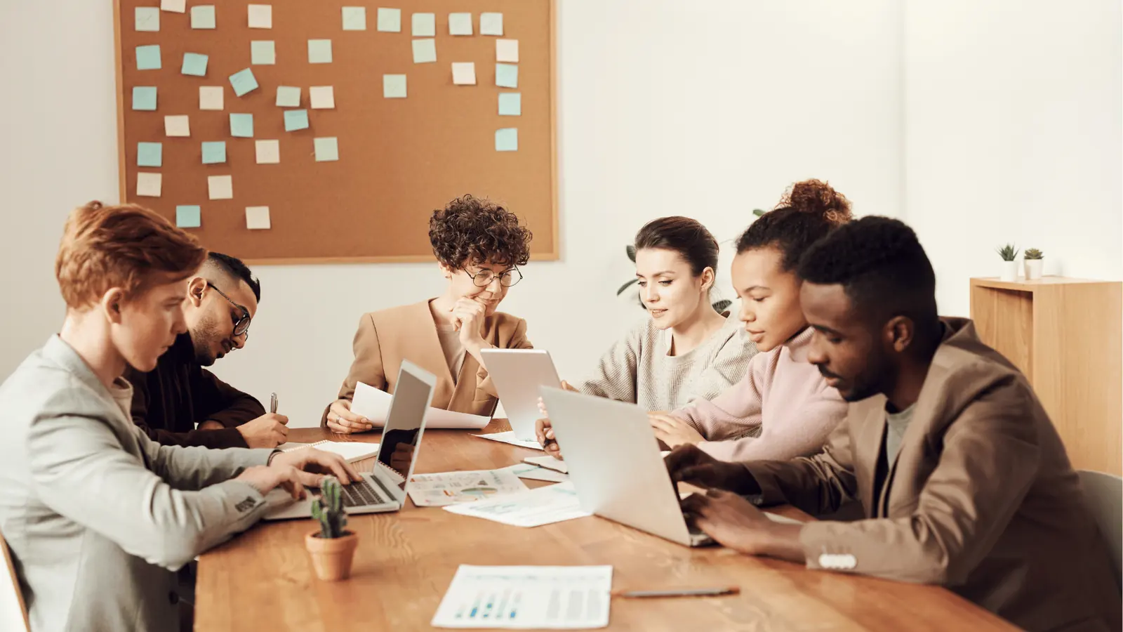 Six colleagues working together at a table with laptops and sticky notes for brand management