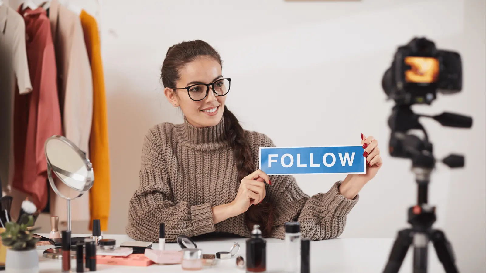 Smiling woman vlogger holds blue FOLLOW sign in front of camera for content calendar