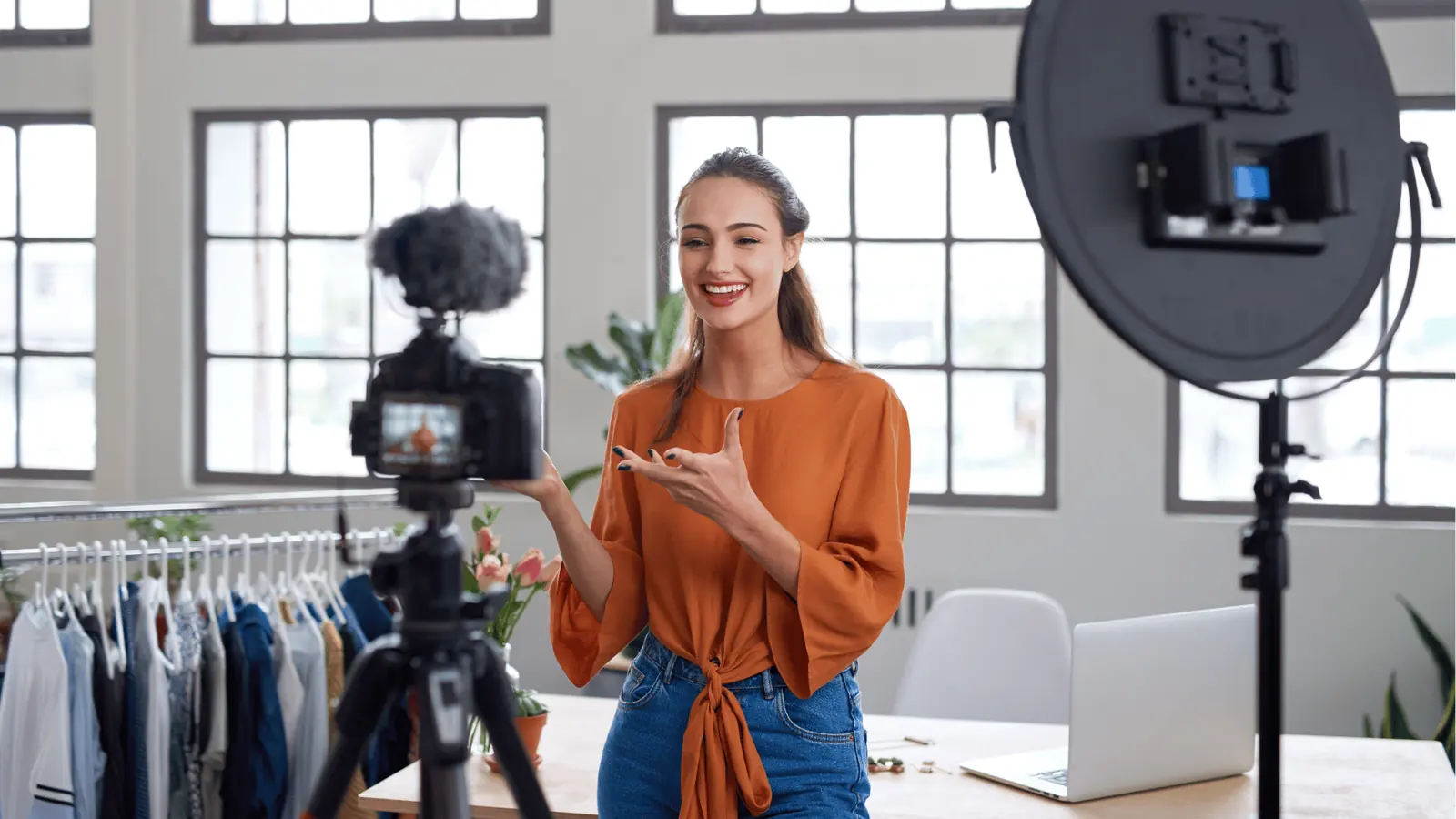 Smiling woman recording a fashion video with camera, ring light, and laptop