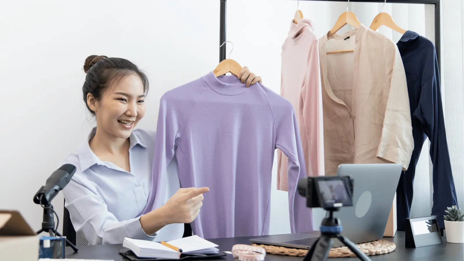 Woman on video showing a purple sweater to camera in a small studio