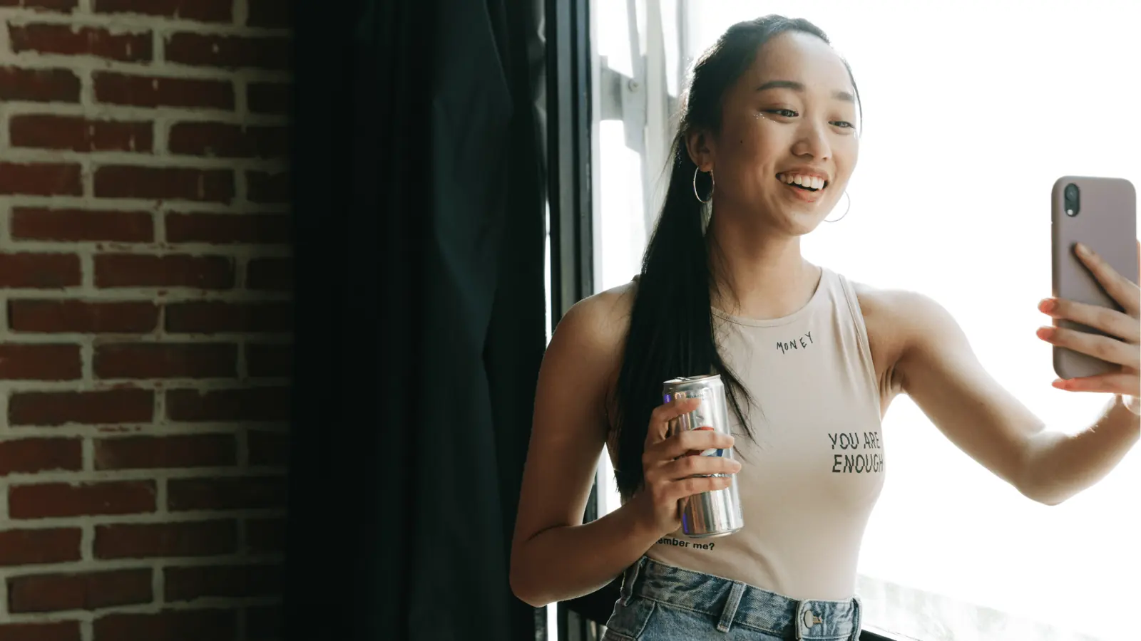 Young woman smiling and taking a selfie while holding a drink