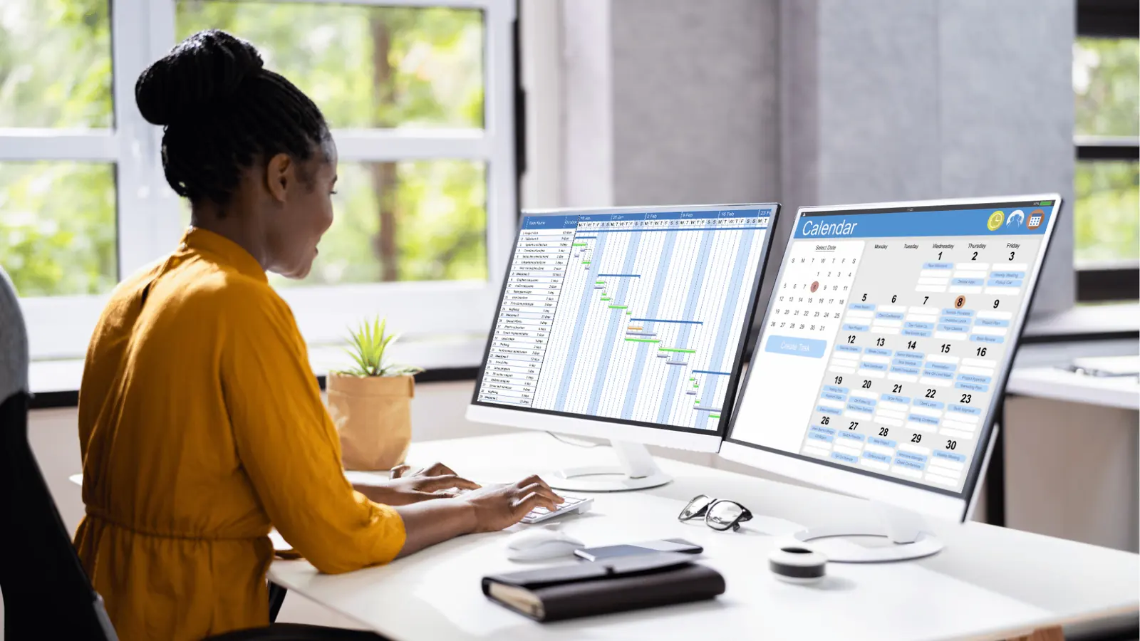 Woman at desk using dual monitors showing calendar and Gantt chart for publishing