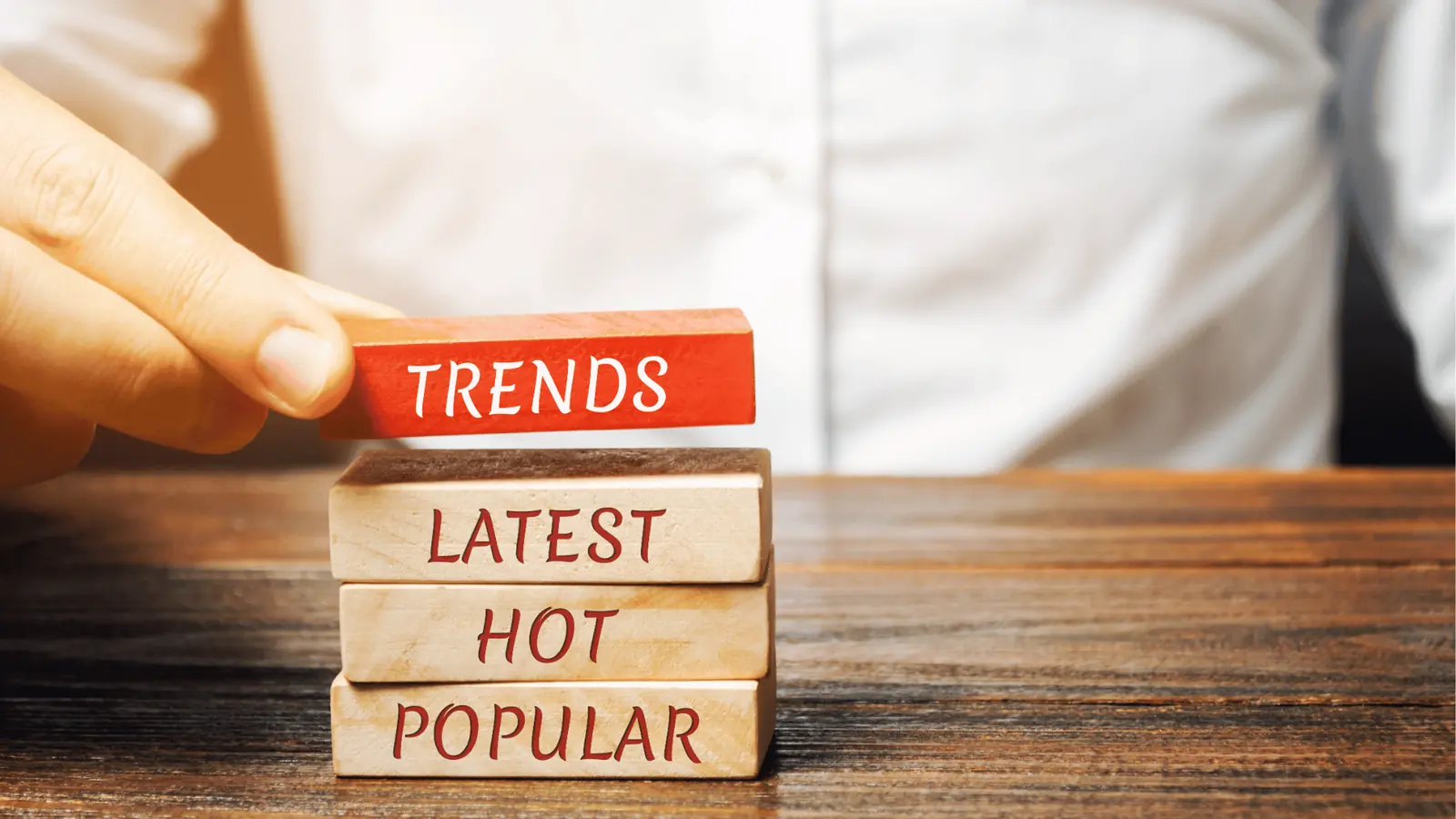 Hand placing a red wooden block labeled TRENDS onto stacked word blocks